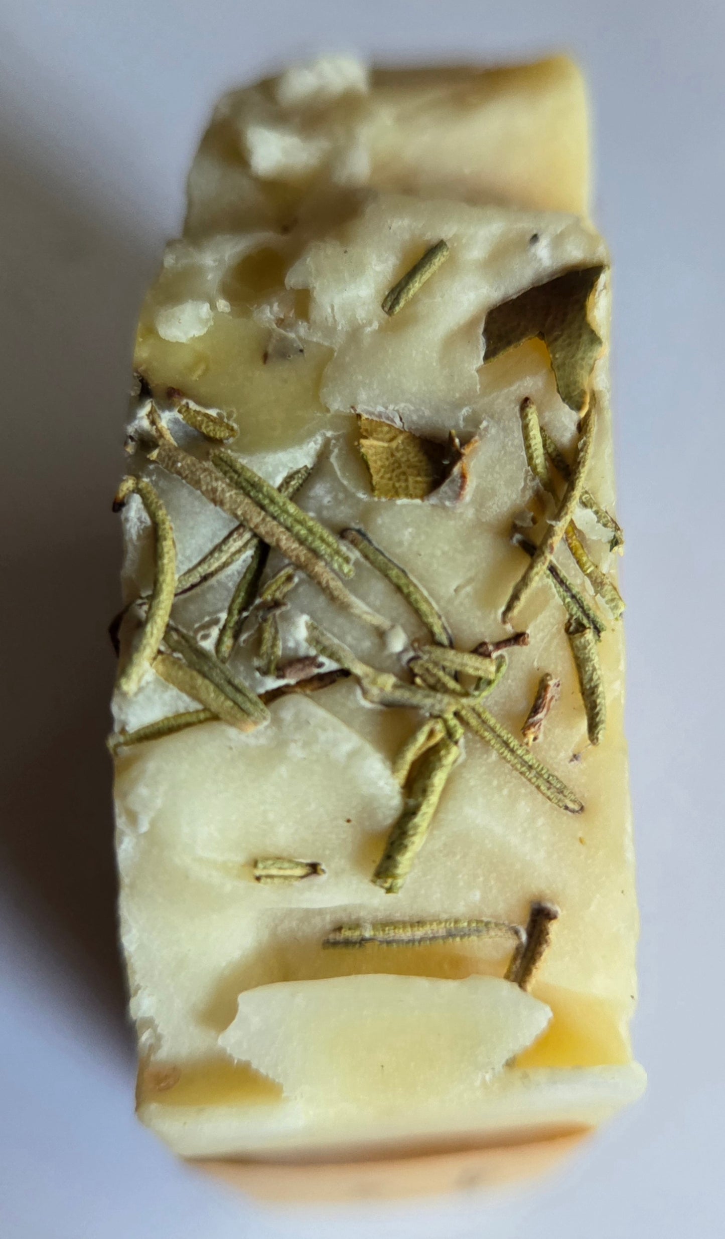 Top view of handmade rosemary soap bar with visible herbs embedded, natural exfoliating skincare product